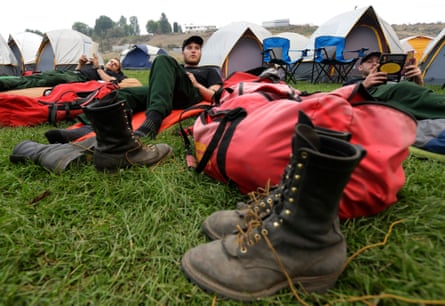 Three men lay down in the grass surrounded by tents, boots and duffle bags