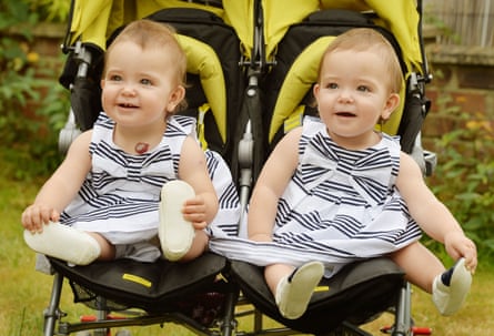 Two babies in a double buggy wearing striped dresses