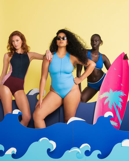 Three models in a blue bikini; a navy and pink zip up swimsuit; and a blue zip up swimsuit