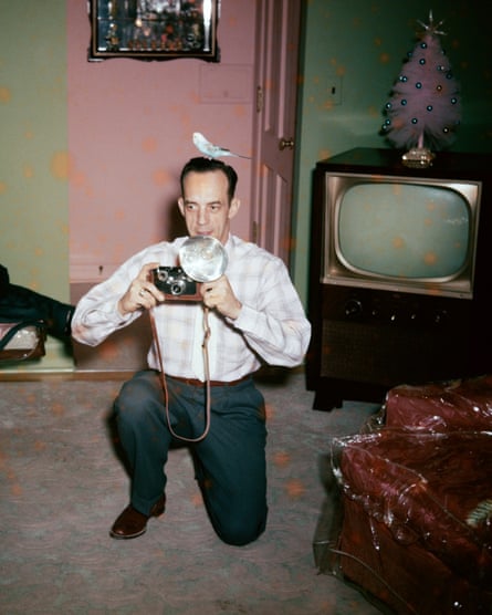 A kneeling man with a bird on head takes a photograph