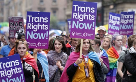 Young women, one with a rainbow flag draped on her shoulders, holding "Trans Rights Now!" placards in the Pride Glasgow parade