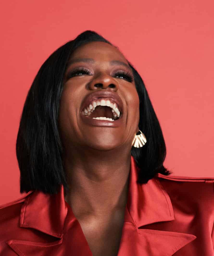 A portrait of Viola Davis wearing an orange satin coat against an orange background