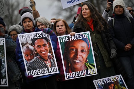 people hold signs that read ‘the faces of foreign aid’ with portraits of people