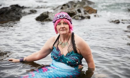 Suzie Inman, with pink hair and in her mermaid outfit, sitting in the sea