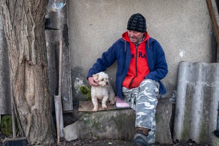 Alexandru Nedelcu, wearing a woolly hat, jacket, hoodie and combat trousers, sits stroking a small dog