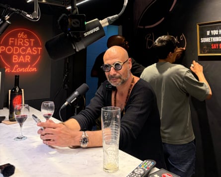 Uri Dinay sits at a bar with a drink, a microphone before him, sound equipment visible