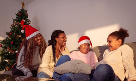 Two women and two children smiling on a sofa wearing Christmas hats 