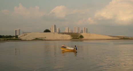 Large piles of sand for land reclamation with high-rise blocks in the distance and a fisher in his boat in the foreground.