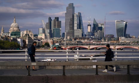 Commuters walk along Waterloo Bridge, against the backdrop of the skyline of the City of London