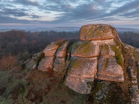 A rocky outcrop, with a metal staircase on it, with trees and hills in the background