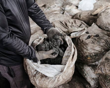 A man stands with his hands in a sack containing a black substance