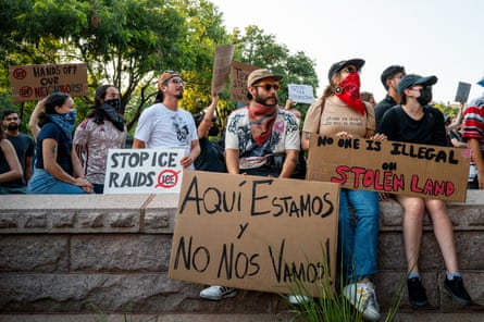 People are shown sitting on and standing behind a wall holding banners and shouting