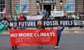 Three people stand on a street holding a banner saying: 'No more climate betrayals'. Other people hold a variety of banners saying: 'Scrap fossil fuels not targets', 'No future in fossil fuels', and 'Scottish Borders for climate justice'