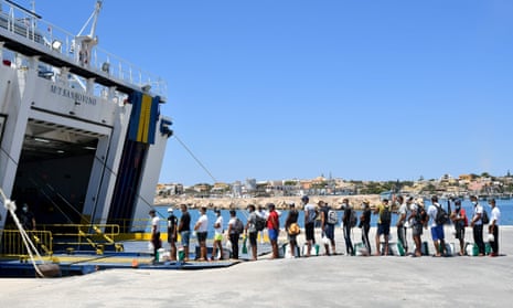 Migrants escorted by police board a ferry on the Italian island of Lampedusa.