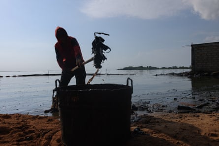 A fisher throws crude oil in a bucket while cleaning the shore of Lake Maracaibo, one of South America’s largest lakes.
