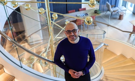 Man looks at camera with hands clasped on spiral stair with molecular model behind