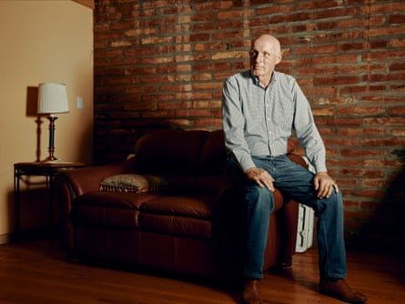 A man in a blueshirt and jeans sitting on a leather couch