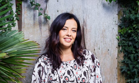 Liz Bonnin stands in front of wood panelling, framed by tall plants.