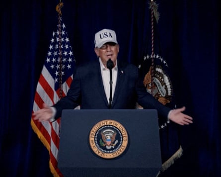 Donald Trump standing at a lectern in a white USA baseball cap