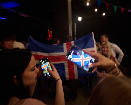 People take photos on their phones of other people waving an Icelandic flag