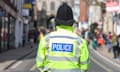 A police officer in a high-viz uniform and black helmet stands on a street, photographed from behind