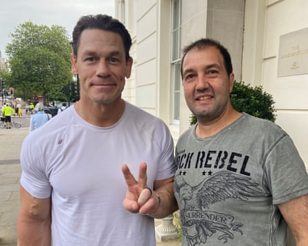A photo of Jason Thanos standing next to John Cena, who holds up a peace sign to the camera.