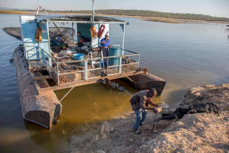 A woman looks on as a young man anchors a fishing boat made of a covered platform between two metal floats 