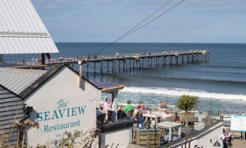 People sitting outside the Seaview Restaurant with Saltburn pier in the background, North Yorkshire, England, UK<br>2GMD466 People sitting outside the Seaview Restaurant with Saltburn pier in the background, North Yorkshire, England, UK