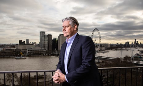 Portrait of John Lundgren leaning against a balcony railing and looking out to the right of the picture, with the river Thames and the London Eye behind him