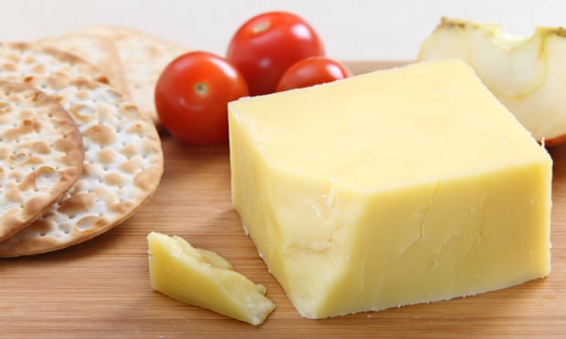 Wedge of cheddar cheese on board with crackers and cherry tomatoes