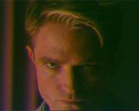 Robert Pattinson's face lit in colorful, high-contrast light in a scene from Primetime