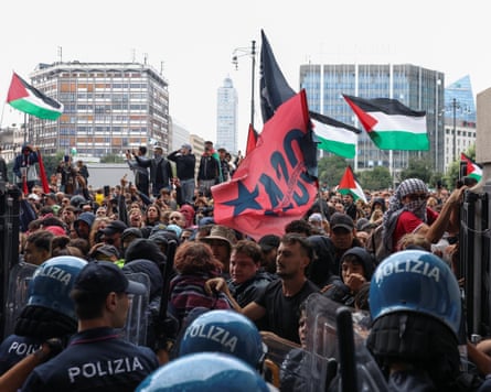 Policías antidisturbios con casco azul de espaldas a la cámara y una multitud de manifestantes detrás de ellos.