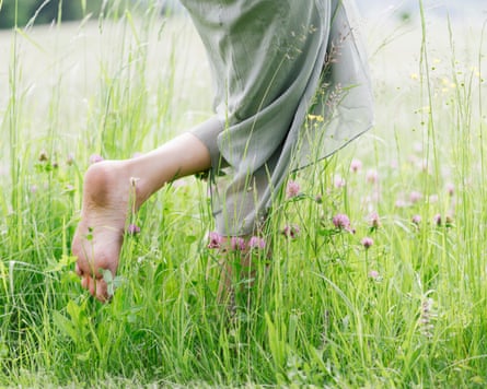 (Legs of) a woman in green skirt running barefoot through long grass and wold flowers