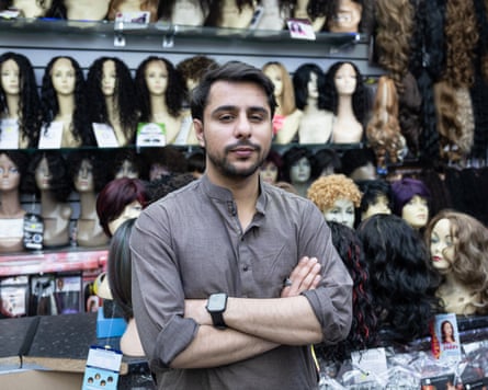 Hassan Naeen stands in front of a display of wigs on mannequin heads