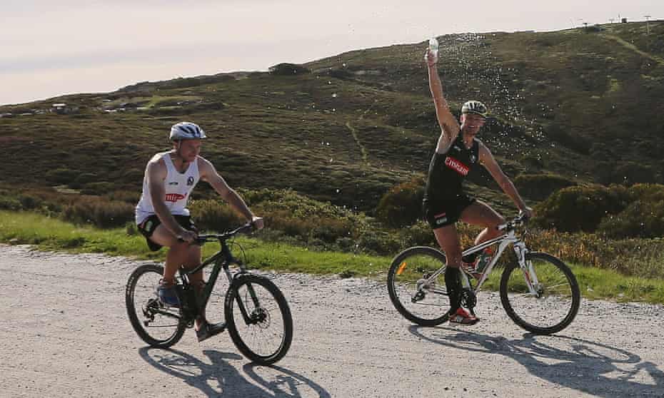 Two men on mountain bikes, one spraying water over himself