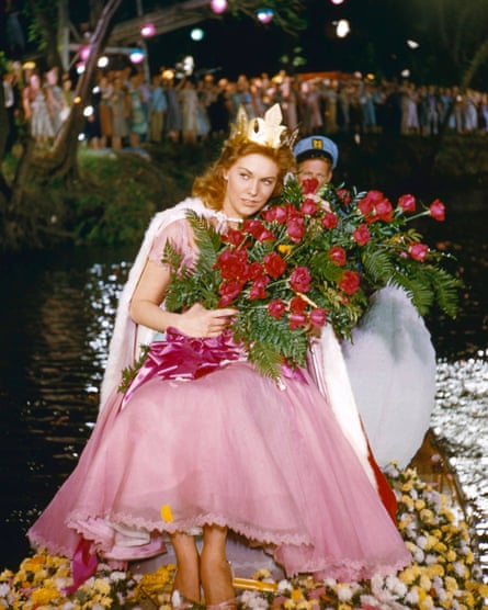 Novak, wearing a pink dress and gold crown, holds a large bunch of red roses.