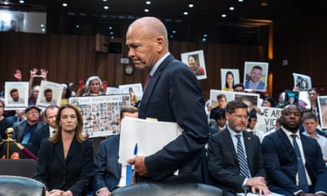 a man walks to his seat in front of people holding up pictures of their dead loved ones