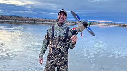 A man stands in front of a lake holding a replica duck