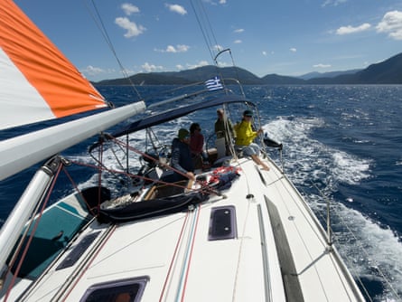 Persone sedute a prua di una barca a vela con un'isola di fronte