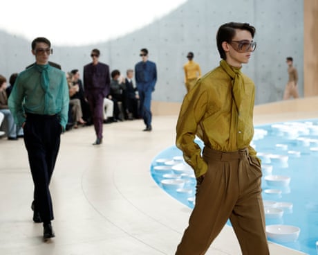 A group of models in sunglasses walk around a curved runway