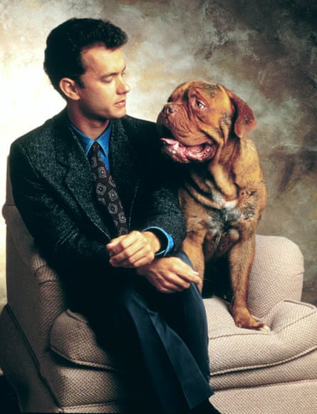 Tom Hanks sits beside Hooch, a large brown dog, perched on a sofa armrest