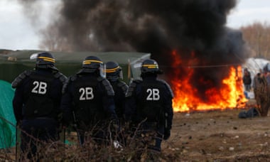 French riot police stand by a burning shelter during the demolition of part of the Jungle migrant camp.