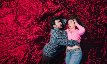 A trick photograph showing Natalie Palamides, with overgrown stubble and in a man's shirt, hugging the waist of a version of herself in a cropped shirt and jeans, hand on her head, both against a crushed velvet background