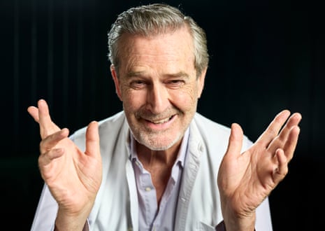 Rupert Everett smiles as he spreads his hands wide, mid-anecdote