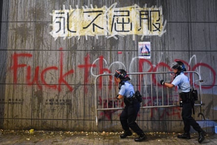 Police remove barricades under a poster displayed on a wall with remnants of thrown eggs and graffiti sprayed by protesters outside the police headquarters in Hong Kong early on June 22, 2019.