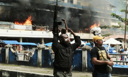 A police officer raises his rifle as the local market is seen burning during a protest in Fakfak, Papua province, Indonesia on 21 August.