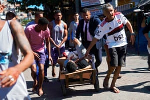 A wounded man is carried on a wheelbarrow by local residents