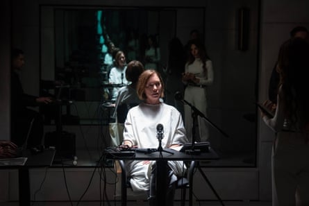 A seated Samantha Redmond wearing a white gown speaks into a microphone on a darkened stage