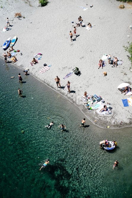 Aerial view of sandy beach ad clear, green water with bathers standing and swimming.
