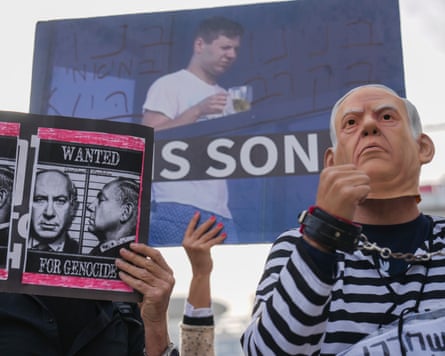 people hold up placards including one with Netanyahu's face on a poster which reads Wanted for Genocide; one person wears a mask resembling his face plus a striped prison-style outfit and a chain around their neck